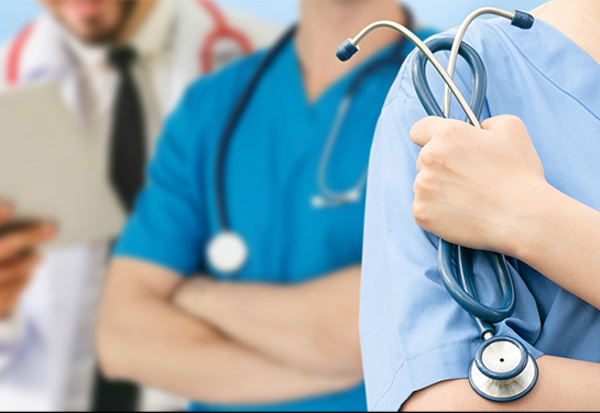 Cropped photo of torsos of three medical professionals with stethoscopes; two are wearing blue scrubs, one has a white lab coat