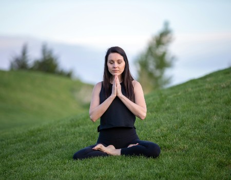 Woman with dark hair, sitting in a yoga pose outside in a green field