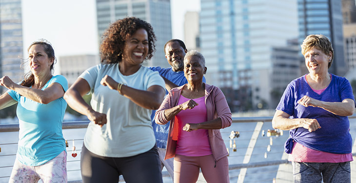 A group of smiling senior adults exercise outdoors in a city.