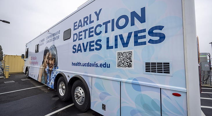 White bus with images of two women and lettering that states “Screening Saves Lives” and “UC Davis Comprehensive Cancer Center”