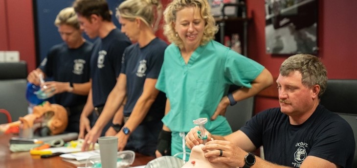 Nurse anesthetist helps firefighters learn how to insert airway device on mannequins. 