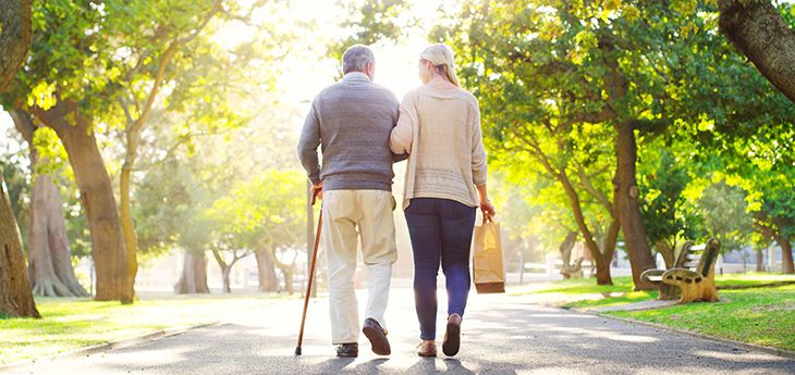  Rearview shot of a young woman assisting her senior father walk at the park