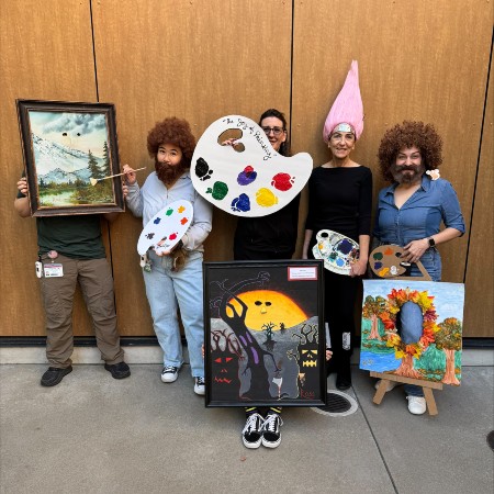 Bob Ross artwork inspired photo with employees wearing big puffy brown wigs and beards