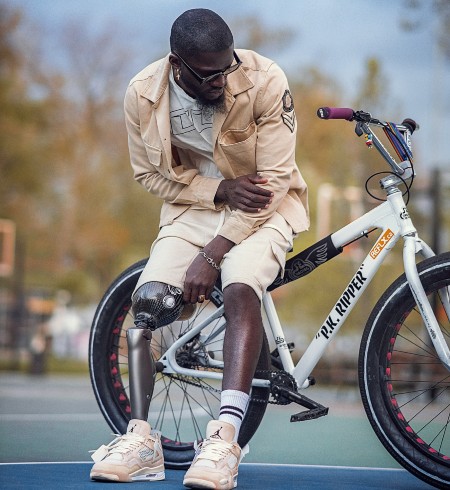 Black man wearing an prosthetic leg, leaning on his bicycle near a skate park