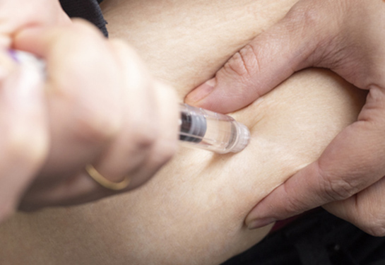 Person self administering a medication using a press injection pen into the abdomen