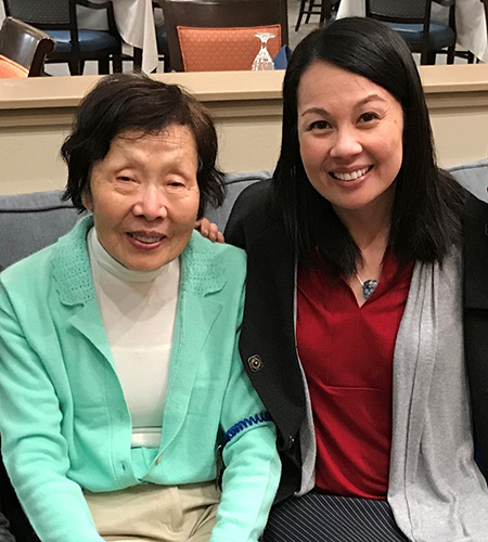 Norika Malhado-Chang is in black jacket, red shirt and grey scarf. Her mother is in teal jacket, white shirt and beige pants.