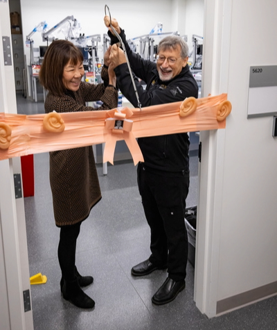 Two people cutting a decorative ribbon at the entrance of a lab.