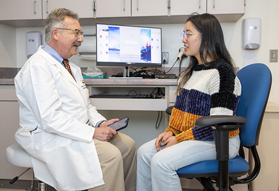 A man in a white coat sits in front of a woman in doctor's office.