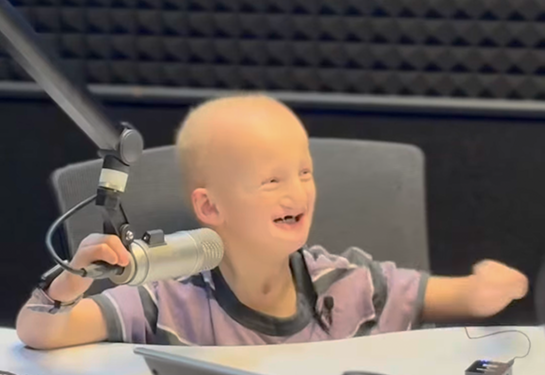 Smiling child talking into a radio studio microphone.