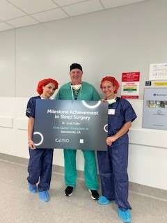 Three people in surgical attire stand in a hallway holding a sign that reads &ldquo;Milestone Achievement in Sleep Surgery.&rdquo;