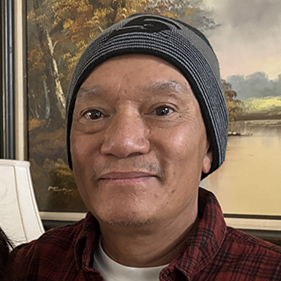 Headshot of Asian man in a red shirt, a white undershirt and a grey beanie.