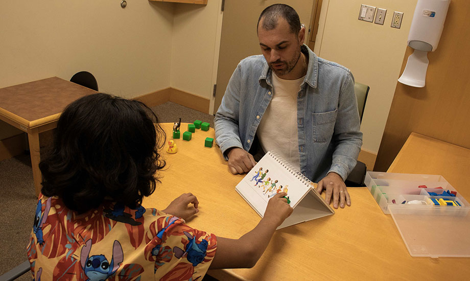 An adolescent boy and a researcher sit at a table doing puzzles