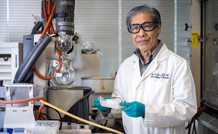Docter Kit Lam smiling in lab holding test tubes