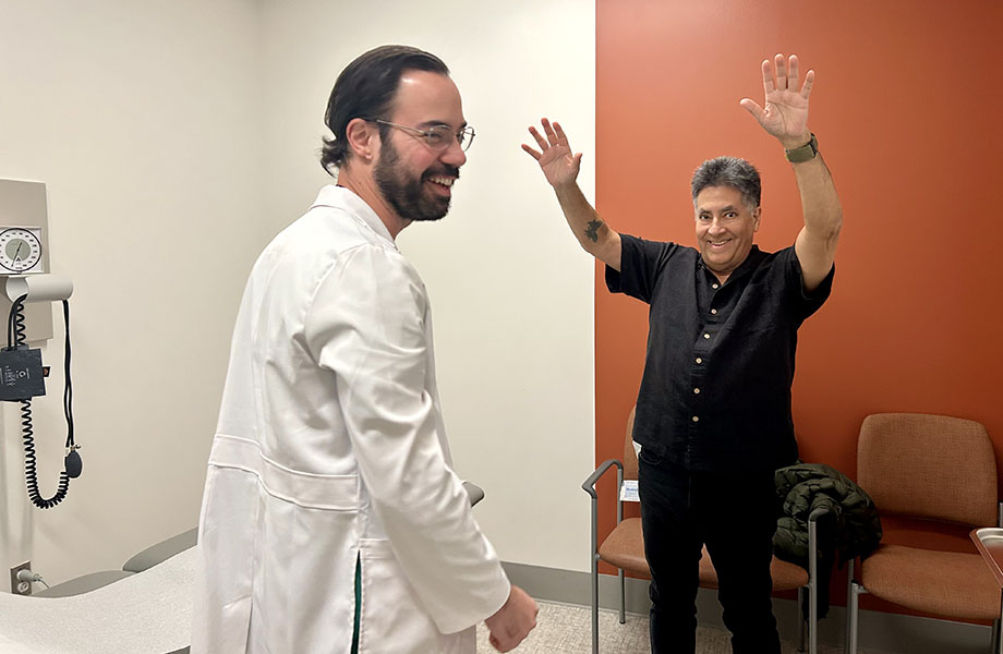 A patient stands with his hands in the air in front of a physician in a white coat.
