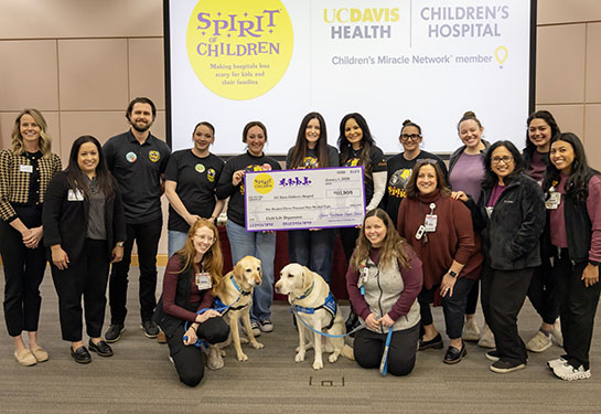 15 people and two dogs surround big check