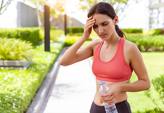 Mujer adulta vestida con prendas para hacer ejercicio tocándose la frente con una mano en señal de dolor o malestar