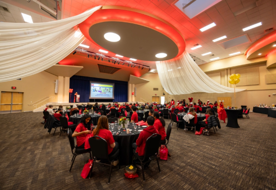 Guests gather in a large event hall decorated in red and white as they listen to a speaker during a heart‑health forum.