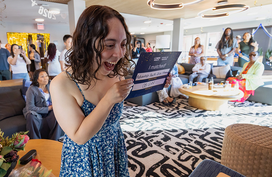 A young woman in a blue floral dress reacts to her match during a video broadcast with fellow classmates