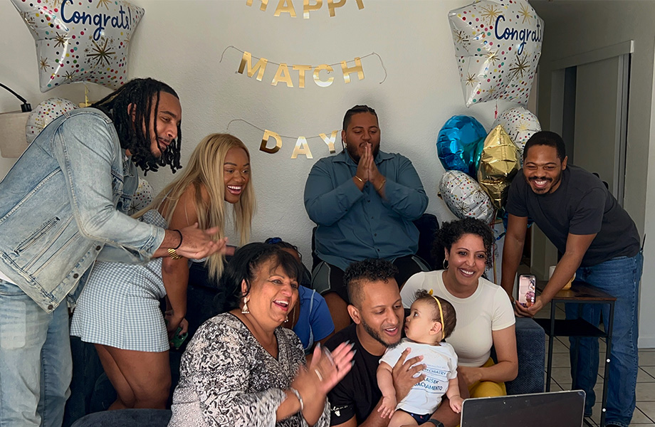 A UC Davis medical student and family celebrate Match Day gathered around a laptop amid balloons and a "Happy Match Day" banner.