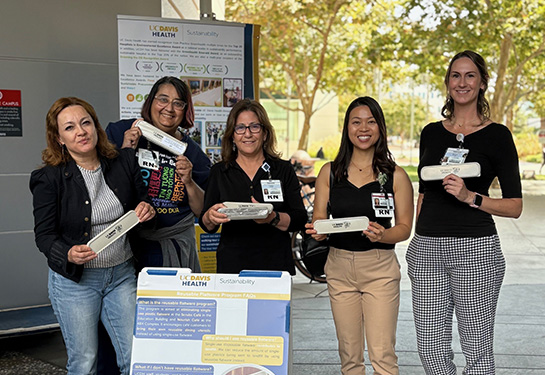 A group of adults stands outside a UC Davis Health building holding reusable utensil cases at a giveaway