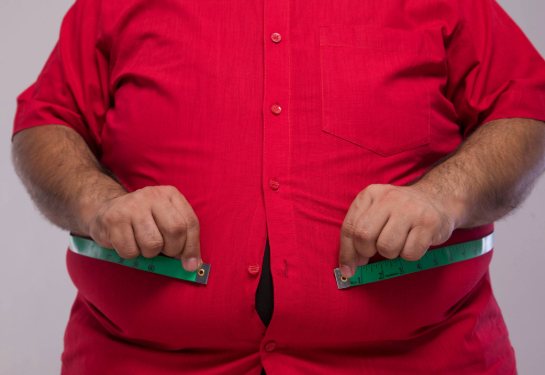 Close up of obese man measuring his overweight stomach with a measuring tape.