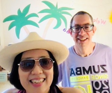 Noriko smiling in front of a palm tree themed Zoom background 