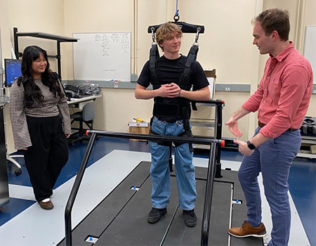 Professor Jonathan Culvert is talking to a person who is supported by safety harness and standing on a rehabilitation treadmill.