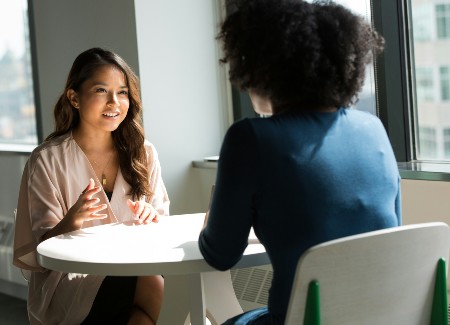 Two women sitting across from each other at a table talking