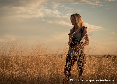 Woman holding a camera while standing out in a field of golden grass