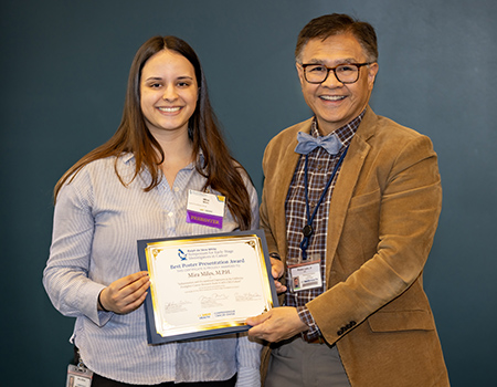 Man standing next to woman with long brown hair, both holding ends of certificate.