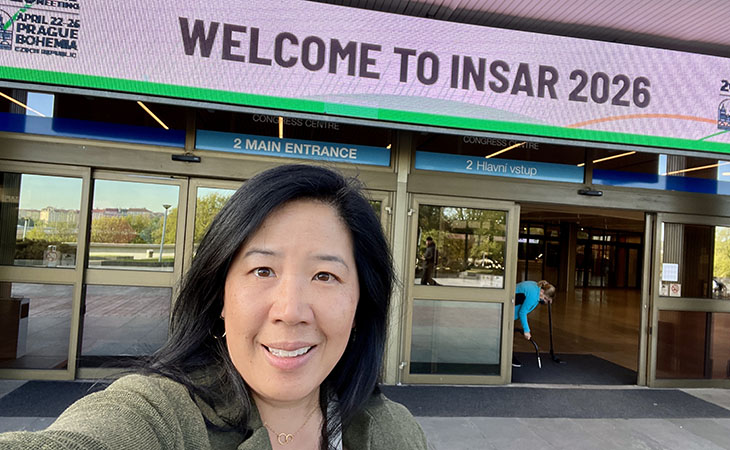 Christine Wu Nordahl poses for a selfie in front of a conference center. A sign above it reads Welcome to INSAR 2026