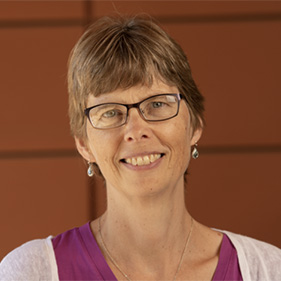 Janine LaSalle, wearing a purple shirt and white sweater and glasses, smiles for the camera. 