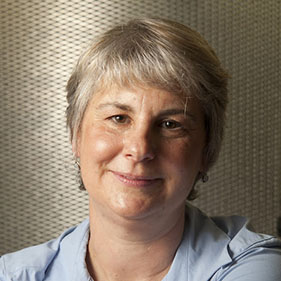 Pamela Lein, wearing a light blue shirt, with short hair, smiles to the camera. 