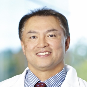 Head-and-shoulders portrait of a medical professional wearing a white coat and tie against a softly blurred background.