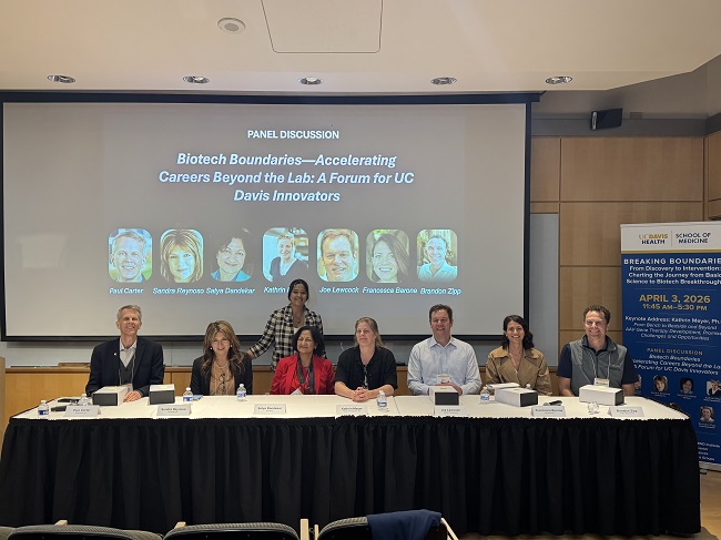 Panel is on stage with name of symposium on the screen behind them.
