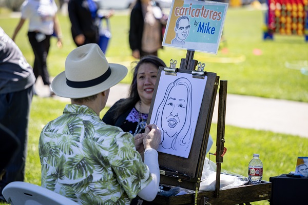 An artist draws a live caricature of an event attendee at an outdoor campus booth.