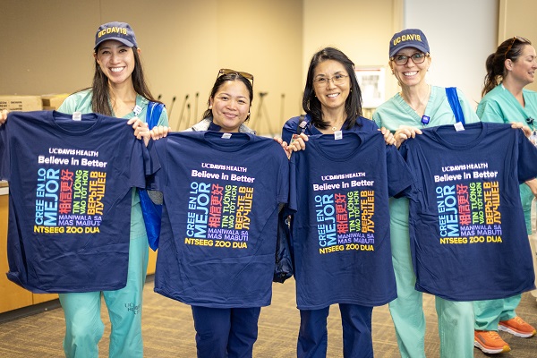 Four healthcare employees stand indoors holding UC Davis Health &ldquo;Believe in Better&rdquo; T-shirts.