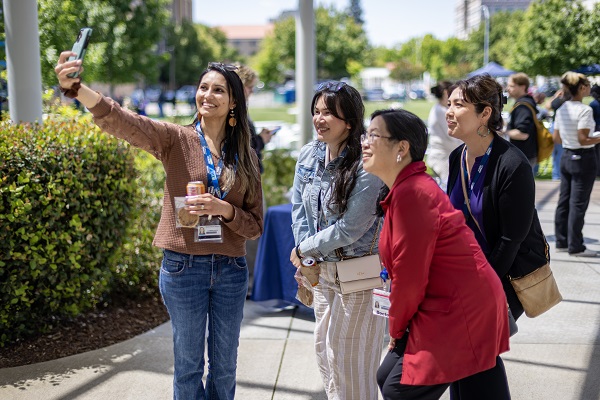 A group of employees pose together for a photo in front of a UC Davis Health event table.