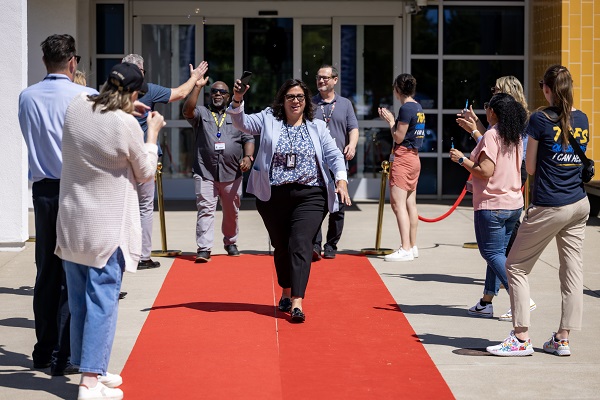 Attendees walk a red carpet outside a UC Davis Health building as colleagues stand on both sides clapping and taking photos.