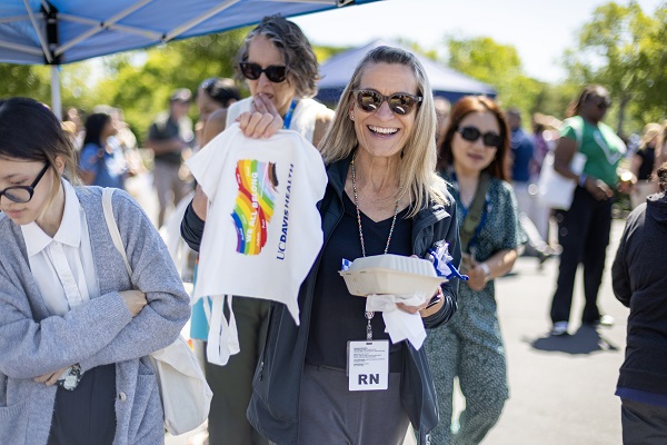 An attendee holds up a white UC Davis Health tote bag with a rainbow logo while carrying a food container.