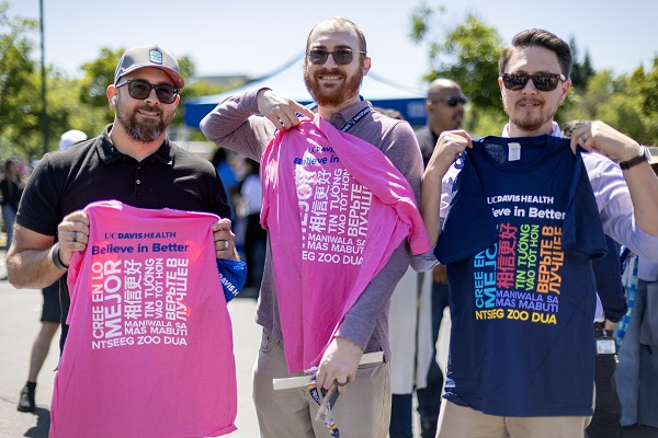 Three attendees hold up UC Davis Health &ldquo;Believe in Better&rdquo; T‑shirts in blue and pink.