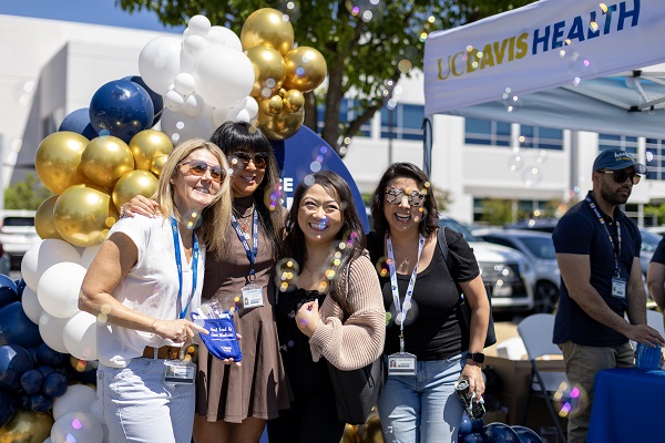 Four attendees pose together in front of a UC Davis Health backdrop decorated with balloons.