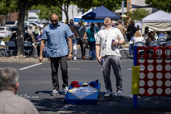 Two attendees play with oversized outdoor games, including cornhole and connect‑four, at an event.