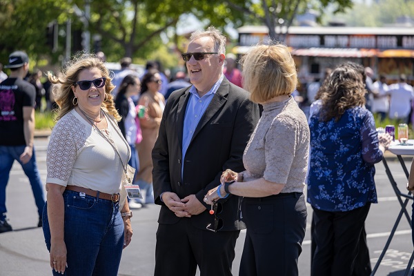 Three attendees stand talking together near food trucks at an outdoor gathering.
