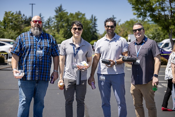 Four attendees walk toward the camera holding food containers and drinks in a parking lot.