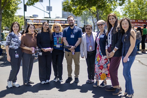 A large group of attendees stands together posing for a group photo with food trucks in the background.