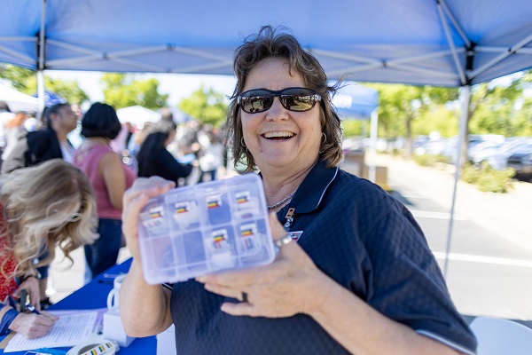 An attendee holds up a small clear container with multiple compartments while standing at a UC Davis Health event table.