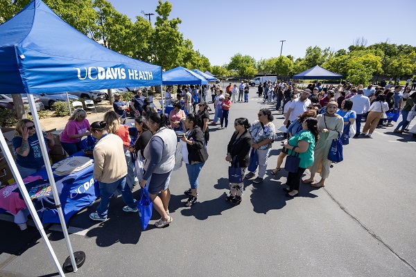 A long line of attendees waits at UC Davis Health tents during an outdoor event in a parking lot.