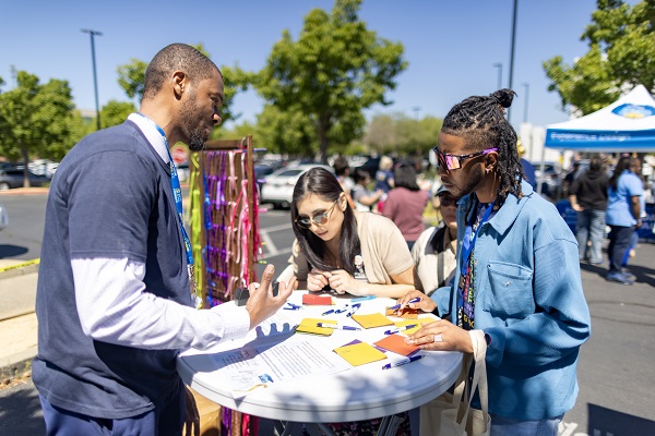 Four attendees stand around a small round table reviewing papers and writing during an outdoor activity.