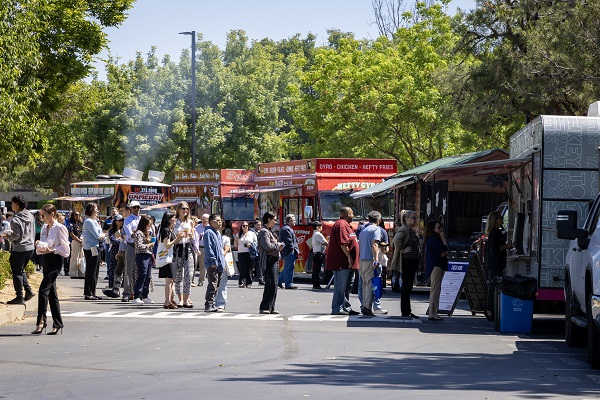 Attendees stand in line at multiple food trucks parked along a tree‑lined area.